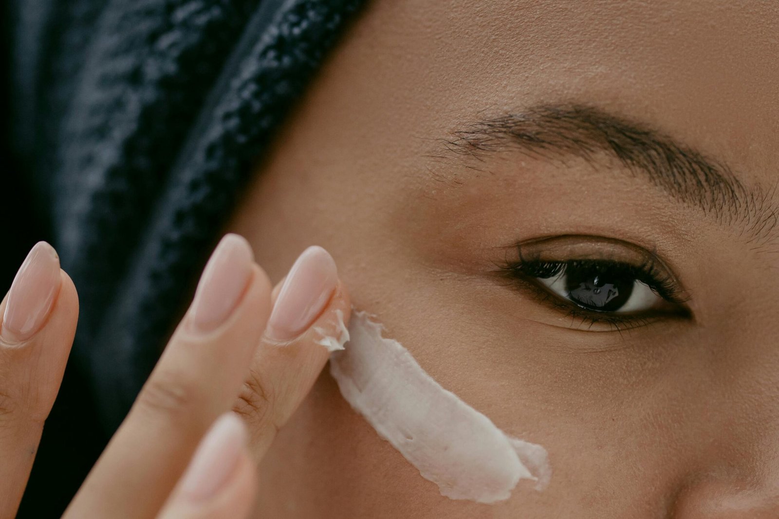 Home Extreme close-up of a woman applying cream to her cheek for healthy skin care.